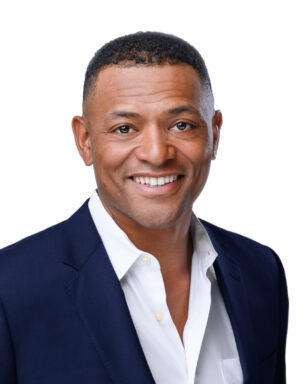 Professional headshot of a smiling man in a navy suit and white shirt against a white background.